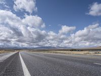 an empty highway in front of mountains under a blue sky filled with clouds during the day