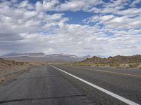 an empty highway in the desert with mountains and sky above it and clouds overhead on a bright, cloudy day