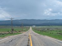 an open road leading toward mountains, a green valley and a white fence line across it