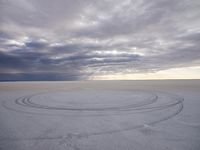 tire marks made in the snow at low tide by dark clouds and a bright white sun