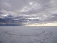 tire marks made in the snow at low tide by dark clouds and a bright white sun