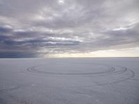 tire marks made in the snow at low tide by dark clouds and a bright white sun