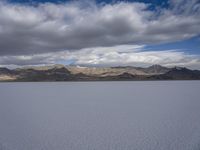 a body of water with hills in the background and clouds in the sky above it