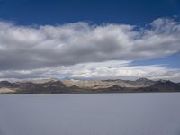 a body of water with hills in the background and clouds in the sky above it