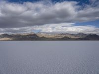 a body of water with hills in the background and clouds in the sky above it