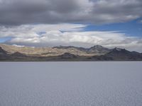 a body of water with hills in the background and clouds in the sky above it