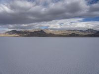 a body of water with hills in the background and clouds in the sky above it