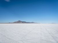 a white desert with some mountains in the distance and sky above it with a small area of snow, a blue sky and small patchy hills