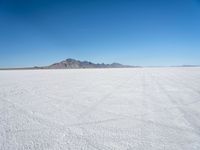 a white desert with some mountains in the distance and sky above it with a small area of snow, a blue sky and small patchy hills