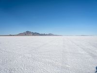 a white desert with some mountains in the distance and sky above it with a small area of snow, a blue sky and small patchy hills