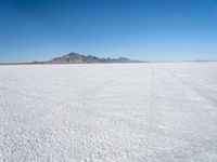 a white desert with some mountains in the distance and sky above it with a small area of snow, a blue sky and small patchy hills