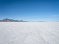 a white desert with some mountains in the distance and sky above it with a small area of snow, a blue sky and small patchy hills