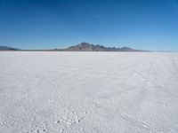 a white desert with some mountains in the distance and sky above it with a small area of snow, a blue sky and small patchy hills