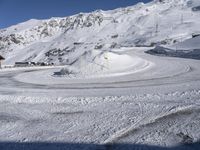 a snowy road with a snow covered mountain in the background with tracks running along it