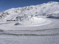 a snowy road with a snow covered mountain in the background with tracks running along it