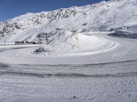 a snowy road with a snow covered mountain in the background with tracks running along it