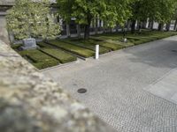 a square concrete courtyard with hedges and trees behind it and some shrubs in a park