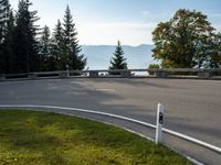 a curved road leading through the woods to mountains in the background with a car driving down it