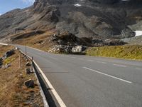 a mountain top road and a single curve on the other side of the mountain are hills with some snow on the tops