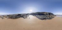 a panorama of a beach in the middle of nowhere next to a cliff with a sun going down on it