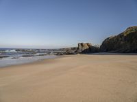 footprints on a sandy beach with some rock and ocean in the background, including an empty bird