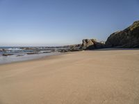 footprints on a sandy beach with some rock and ocean in the background, including an empty bird