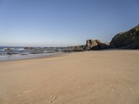 footprints on a sandy beach with some rock and ocean in the background, including an empty bird