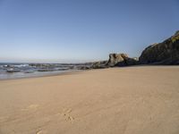 footprints on a sandy beach with some rock and ocean in the background, including an empty bird