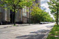 an empty street with green trees on both sides and people walking down the sidewalk on either side