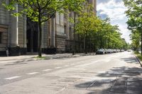 an empty street with green trees on both sides and people walking down the sidewalk on either side