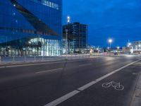 a bike lane that has some buildings on the side of it at night with lights on and traffic on