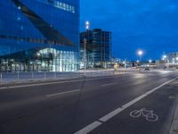 a bike lane that has some buildings on the side of it at night with lights on and traffic on