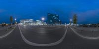 a large parking lot with multiple parking spaces around it in the evening time seen from the road, as it is surrounded by the modern buildings and trees