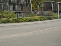 two large buildings on the side of the road with bushes in front of them and a person walking down the sidewalk