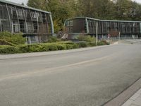 two large buildings on the side of the road with bushes in front of them and a person walking down the sidewalk