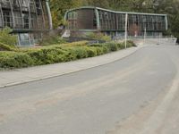 two large buildings on the side of the road with bushes in front of them and a person walking down the sidewalk