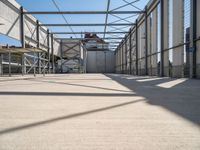 a hallway with a steel roof and many metal columns leading up into the building, on a sunny day