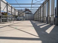 a hallway with a steel roof and many metal columns leading up into the building, on a sunny day