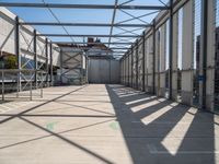 a hallway with a steel roof and many metal columns leading up into the building, on a sunny day