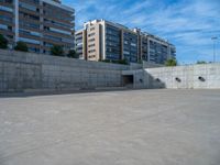 the empty parking lot in front of a wall with apartment buildings on it and a skateboarder on a ramp