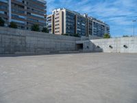 the empty parking lot in front of a wall with apartment buildings on it and a skateboarder on a ramp