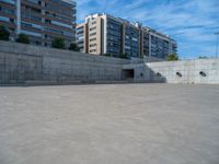 the empty parking lot in front of a wall with apartment buildings on it and a skateboarder on a ramp