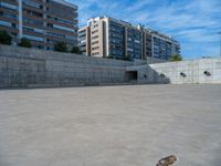 the empty parking lot in front of a wall with apartment buildings on it and a skateboarder on a ramp