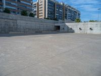 the empty parking lot in front of a wall with apartment buildings on it and a skateboarder on a ramp