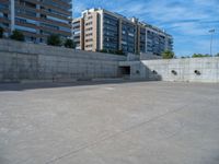 the empty parking lot in front of a wall with apartment buildings on it and a skateboarder on a ramp