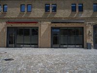 the sidewalk is paved with stones and has a bench in front of it, with no people inside