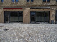 the sidewalk is paved with stones and has a bench in front of it, with no people inside