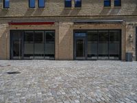 the sidewalk is paved with stones and has a bench in front of it, with no people inside