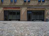 the sidewalk is paved with stones and has a bench in front of it, with no people inside