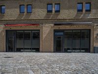 the sidewalk is paved with stones and has a bench in front of it, with no people inside